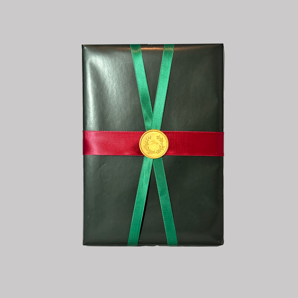 Gift wrap option - gloss black paper with criss-crossed green and red ribbon with a gold laurel leaf seal in the center